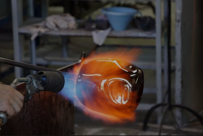 Murano glassblower shaping molten glass in a traditional furnace workshop.