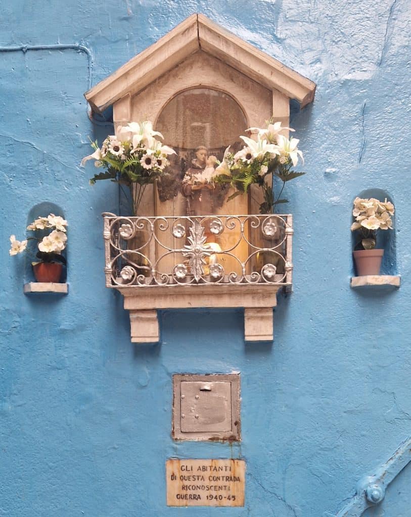 Venetian street shrine with flowers and votive light, dedicated by local residents after World War II.”