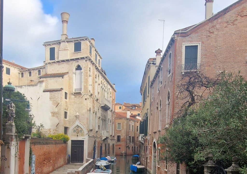 View of a peaceful Venetian canal with historic buildings, boats and traditional chimneys, representing the atmosphere of the Venice travel guides on TripVenice.
